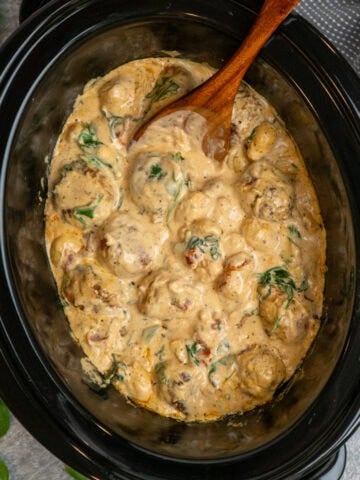 Crock pot Tuscan meatballs with gnocchi and wooden spoon ready to serve.