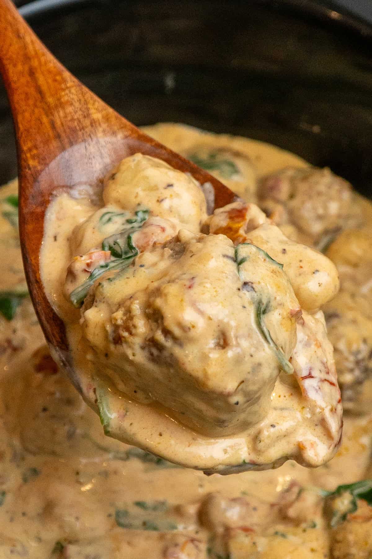 A wooden spoon holding a scoop of Tuscan chicken meatballs with gnocchi.