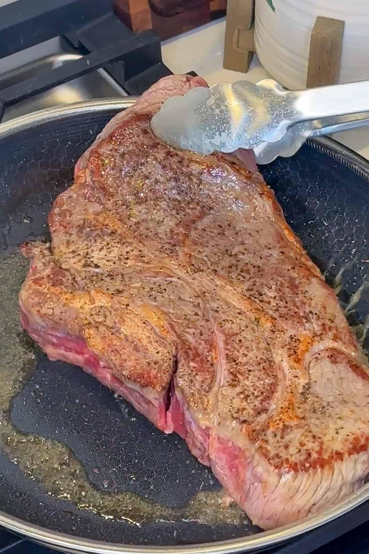A seasoned chuck roast being seared in a skillet.