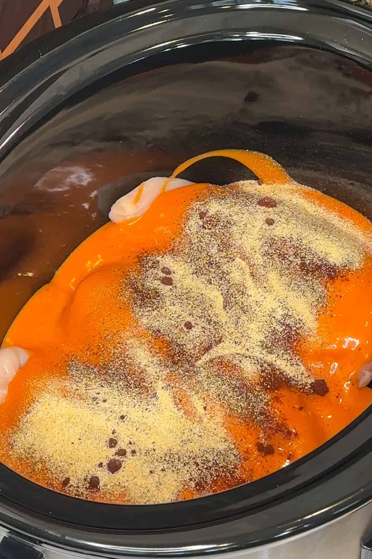 Chicken covered in buffalo sauce and seasonings in a crock pot.