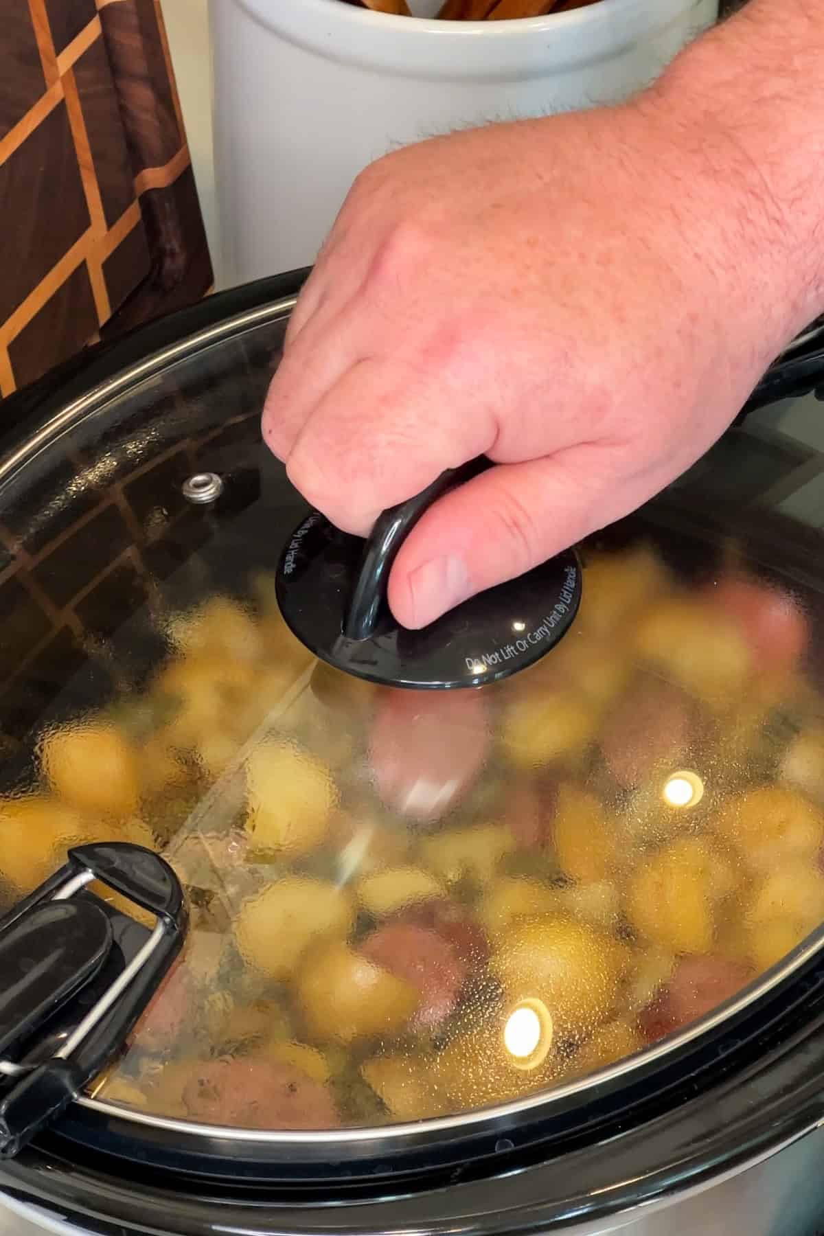 A hand putting on a slow cooker lid so the swamp potatoes can be cooked.
