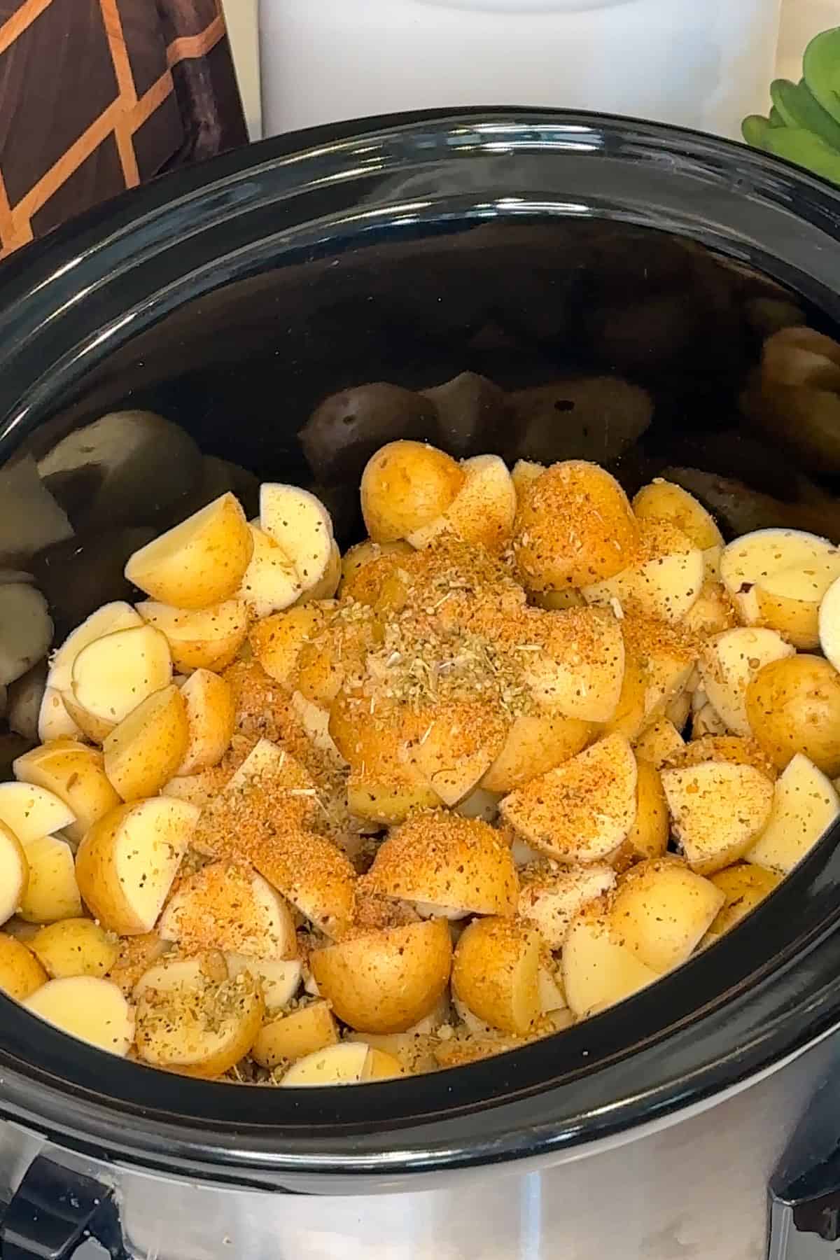 Petite Yukon potatoes in a slow cooker with seasonings on top.