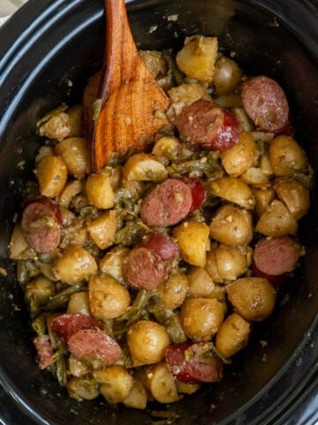 Swamp potatoes in a crock pot with a wooden spoon ready to be served.
