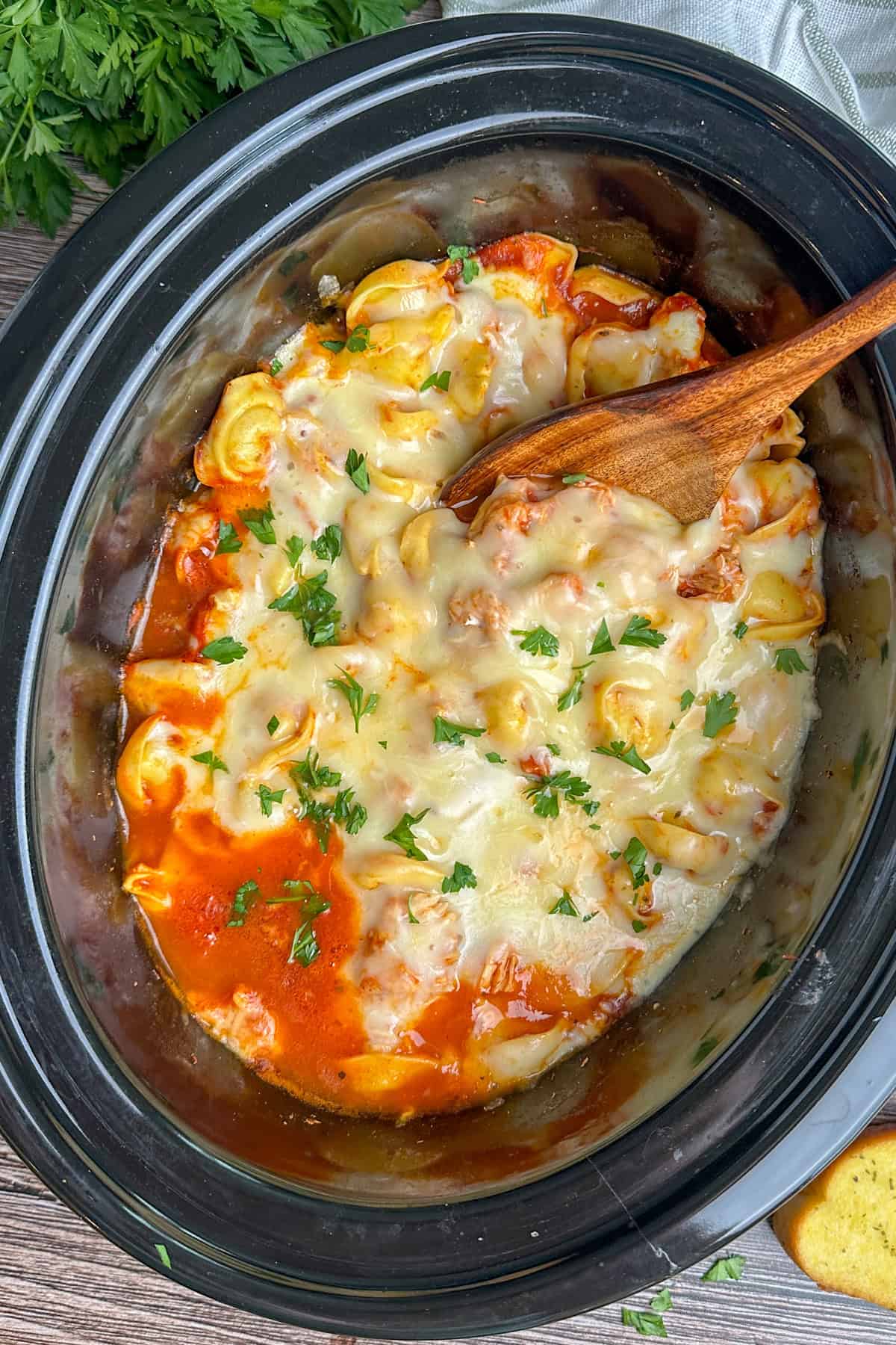 Chicken parmesan tortellini in a crock pot with a wooden spoon.