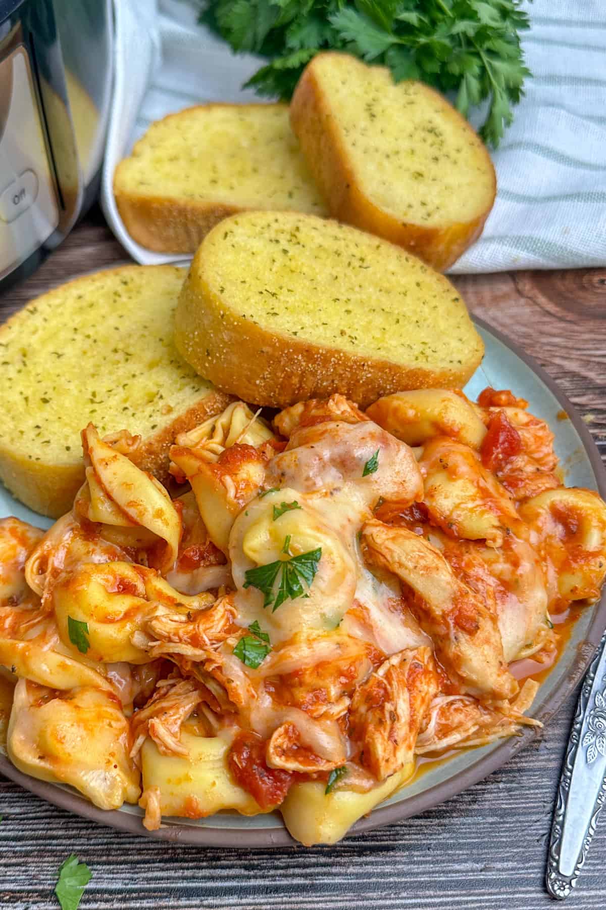 Chicken parmesan tortellini on a plate with two pieces of garlic bread.