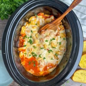 Chicken parmesan tortellini in a crock pot with a wooden spoon.