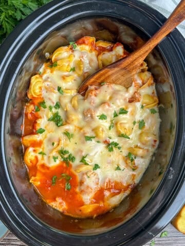 Chicken parmesan tortellini in a crock pot with a wooden spoon.