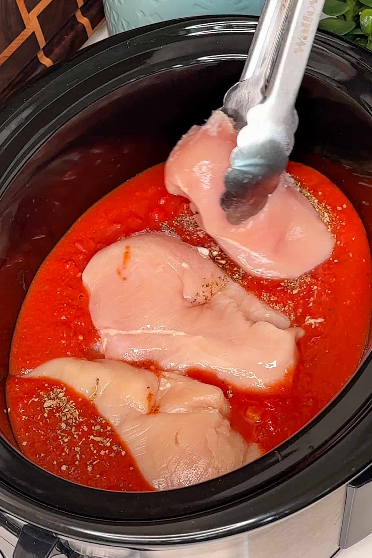 Three chicken breasts added to the sauce in a crock pot.
