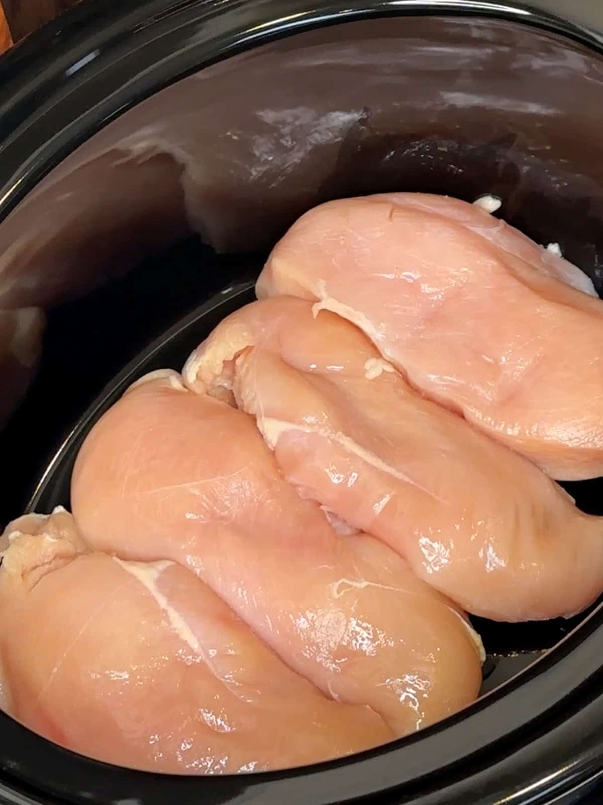 Four chicken breasts in the bottom of a slow cooker.