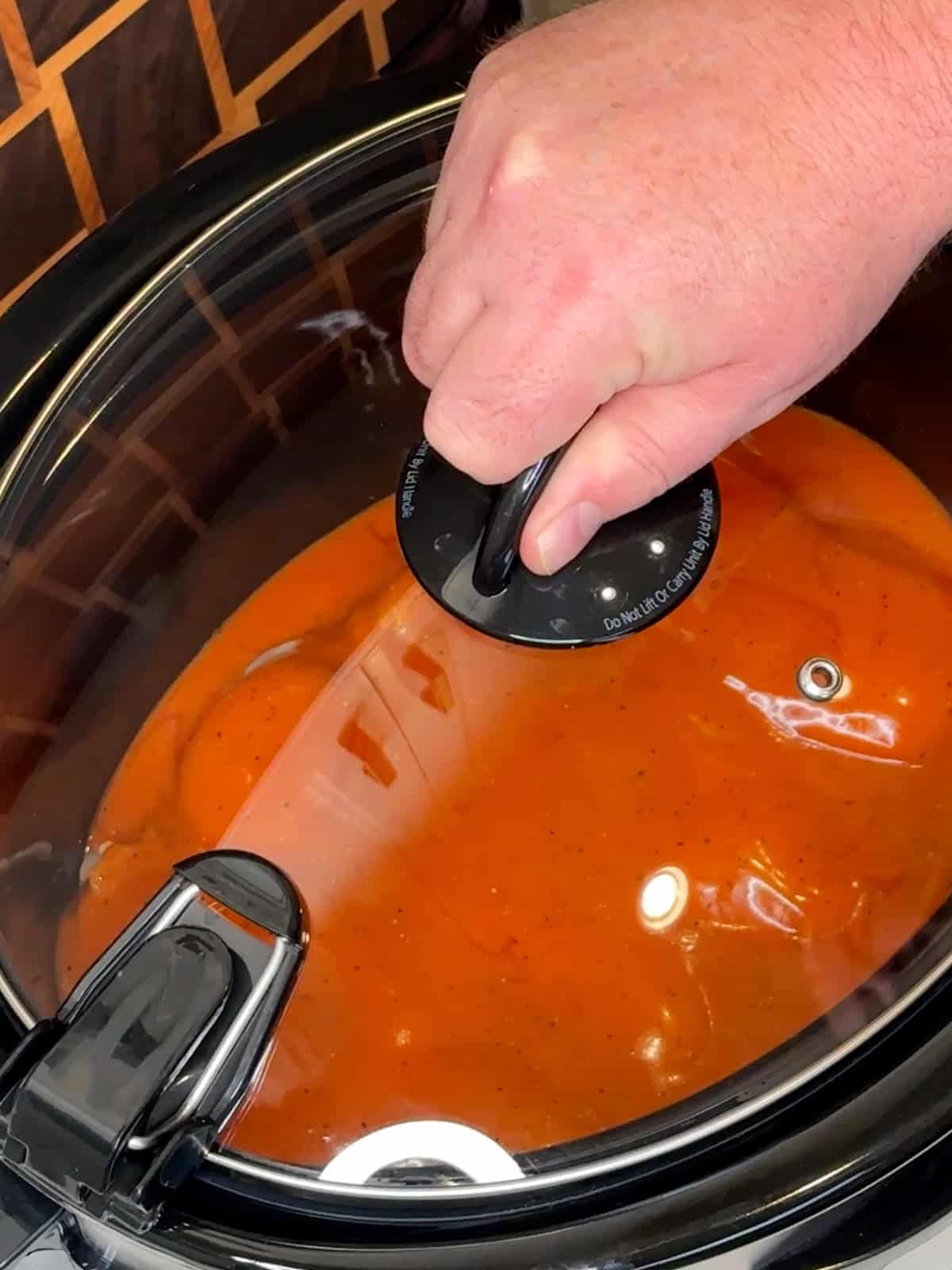 A hand putting a lid on a slow cooker so the recipe can cook.
