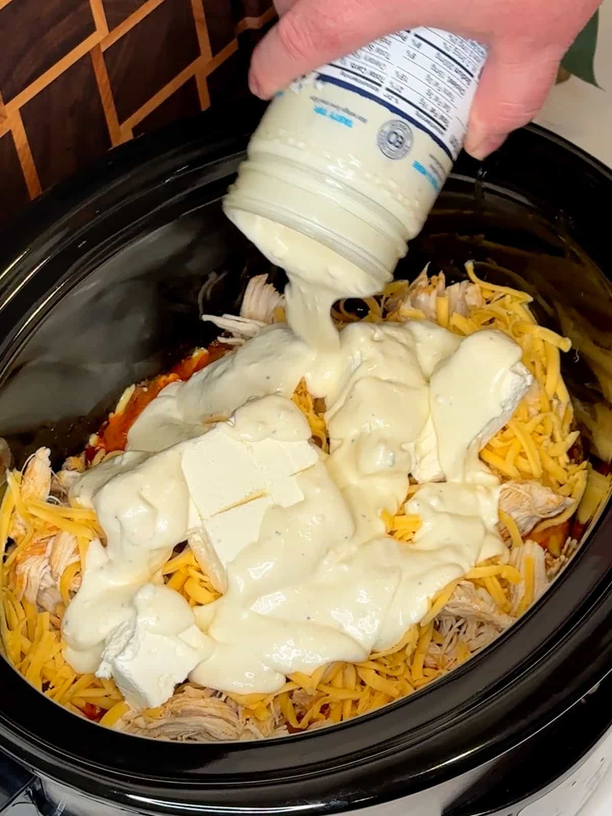 Cheddar cheese, cream cheese and blue cheesing dressing being added to shredded chicken and buffalo sauce.