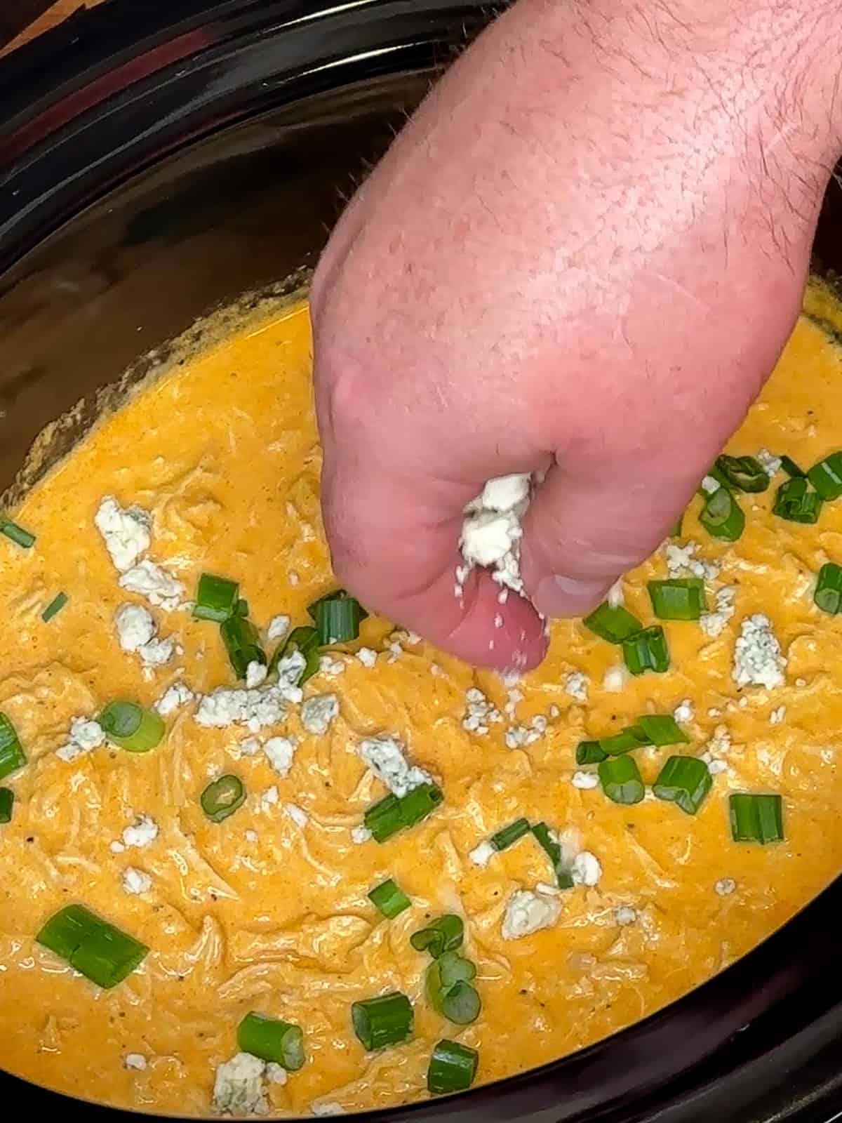 Green onion and blue cheese crumbles being sprinkled over the buffalo chicken dip.