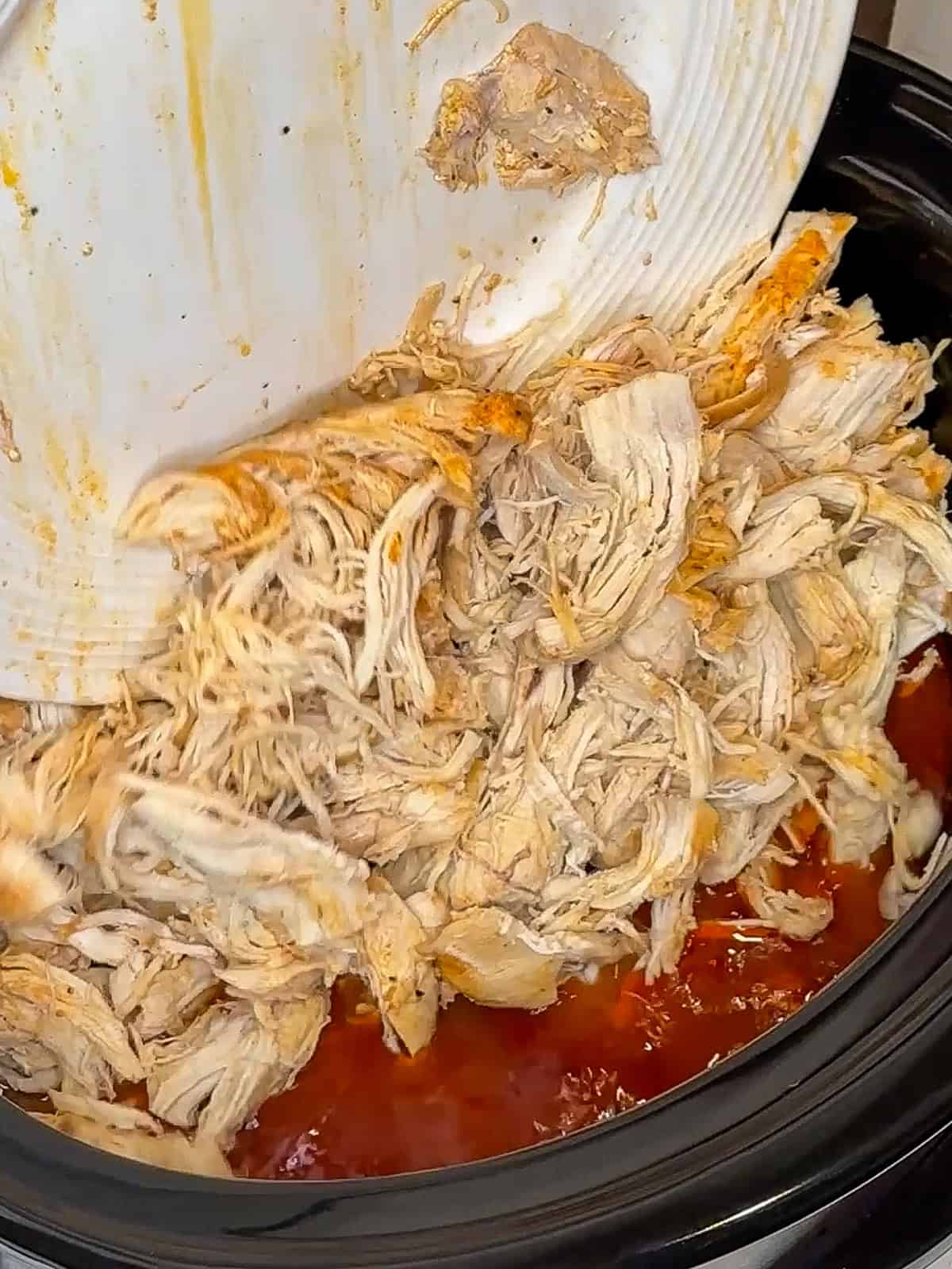 Shredded chicken being added back in the buffalo sauce in a slow cooker.