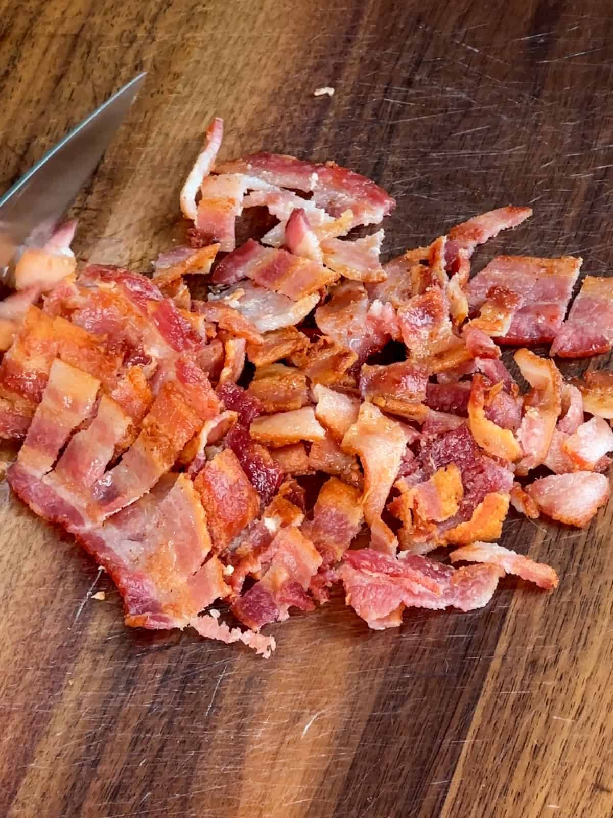 Cooked and chopped bacon on a wooden cutting board.
