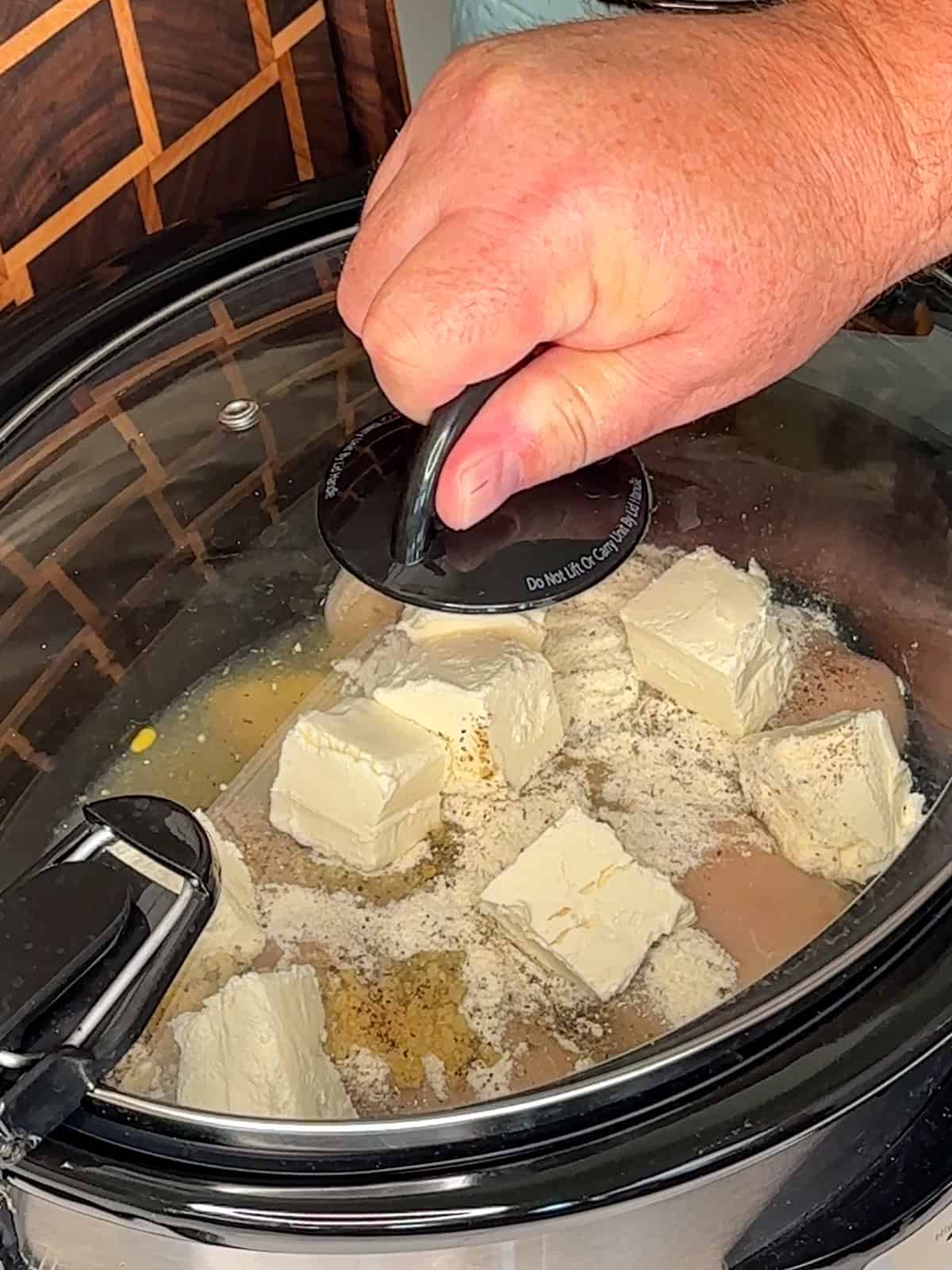 A hand putting a lid on a slow cooker so the crack chicken can be cooked.