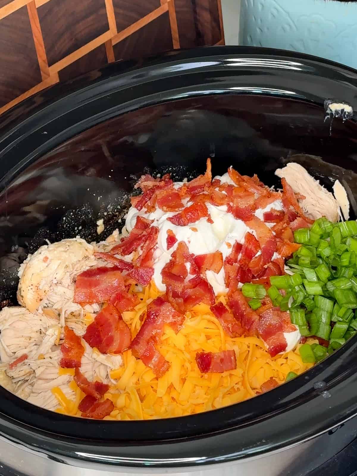 Shredded chicken, cheddar cheese, sour cream, bacon and green onions added to the slow cooker.
