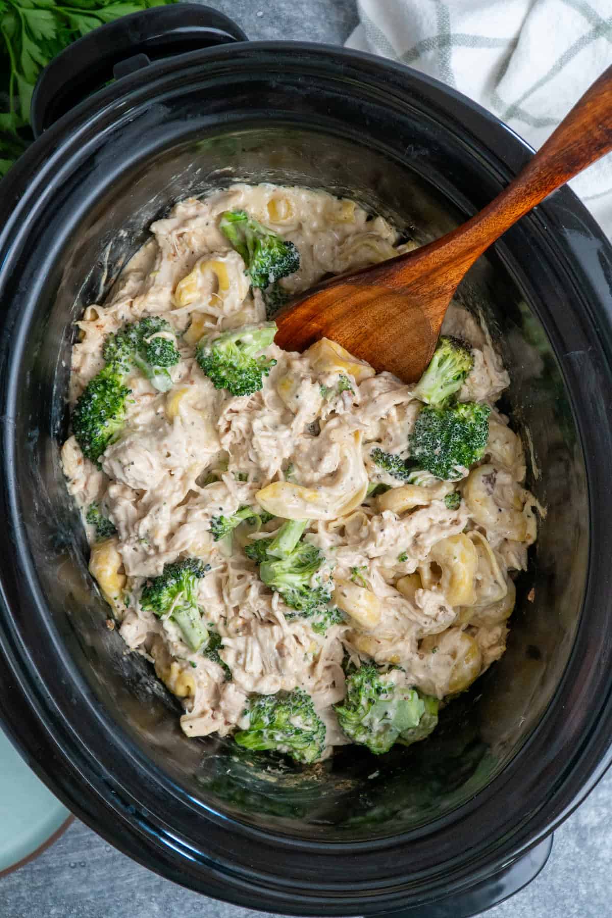 Slow cooker chicken broccoli tortellini with a wooden spoon ready to be served.