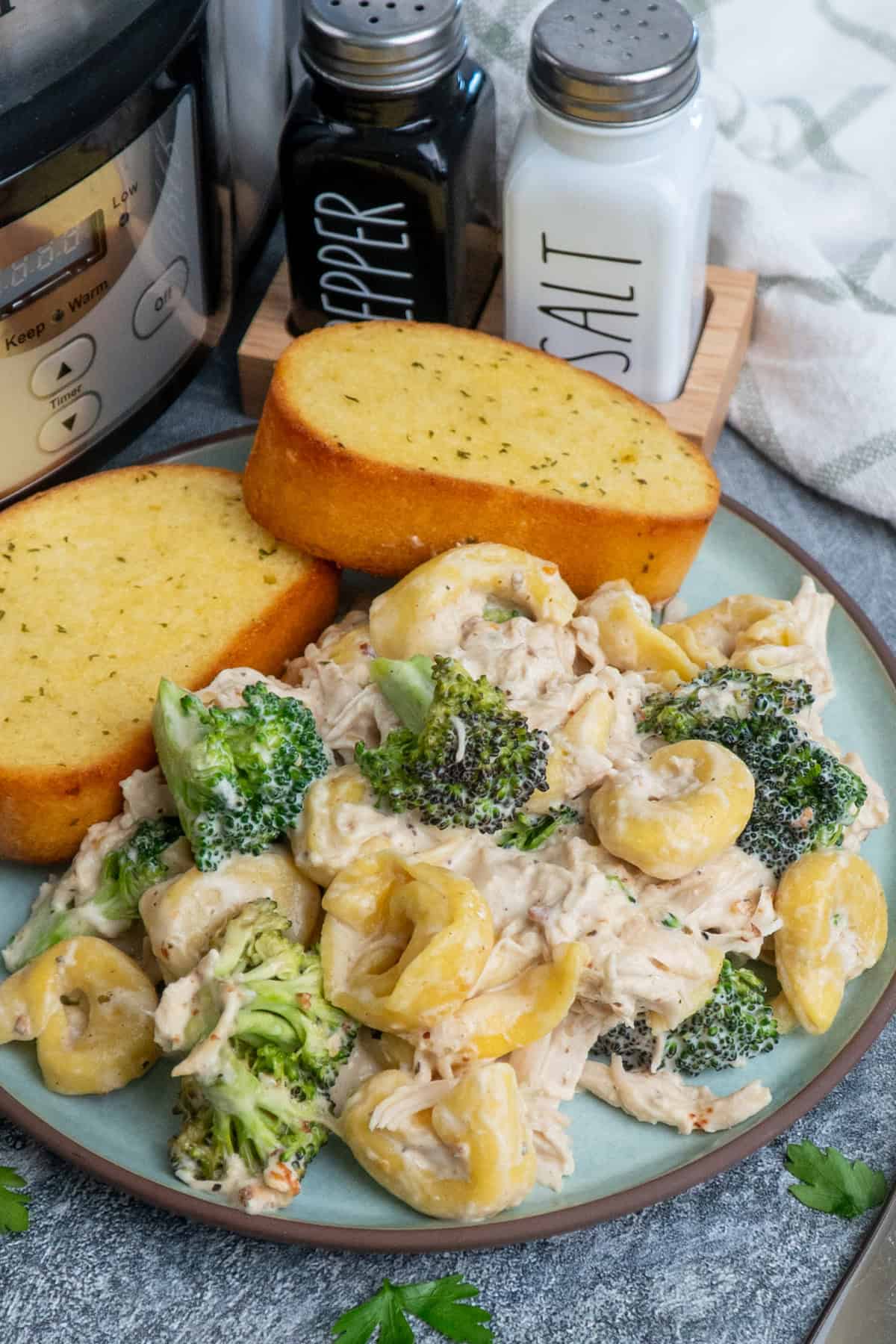 Chicken broccoli tortellini on a plate with two pieces of garlic bread.