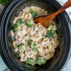 Slow cooker chicken broccoli tortellini with a wooden spoon ready to be served.