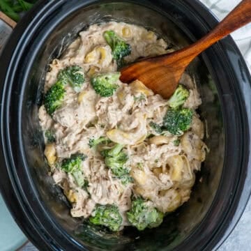 Slow cooker chicken broccoli tortellini with a wooden spoon ready to be served.
