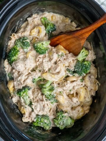 Slow cooker chicken broccoli tortellini with a wooden spoon ready to be served.