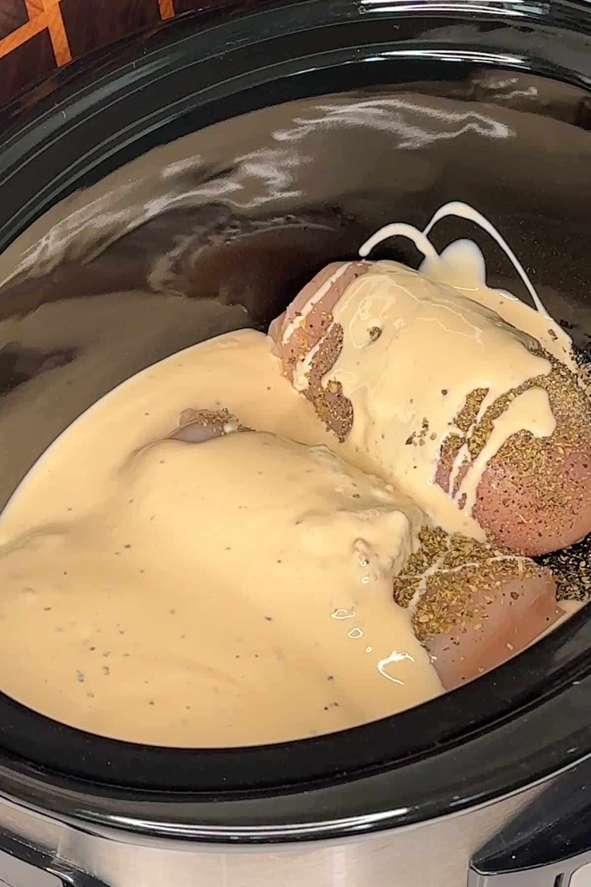 Three chicken breasts in a crock pot covered in alfredo.