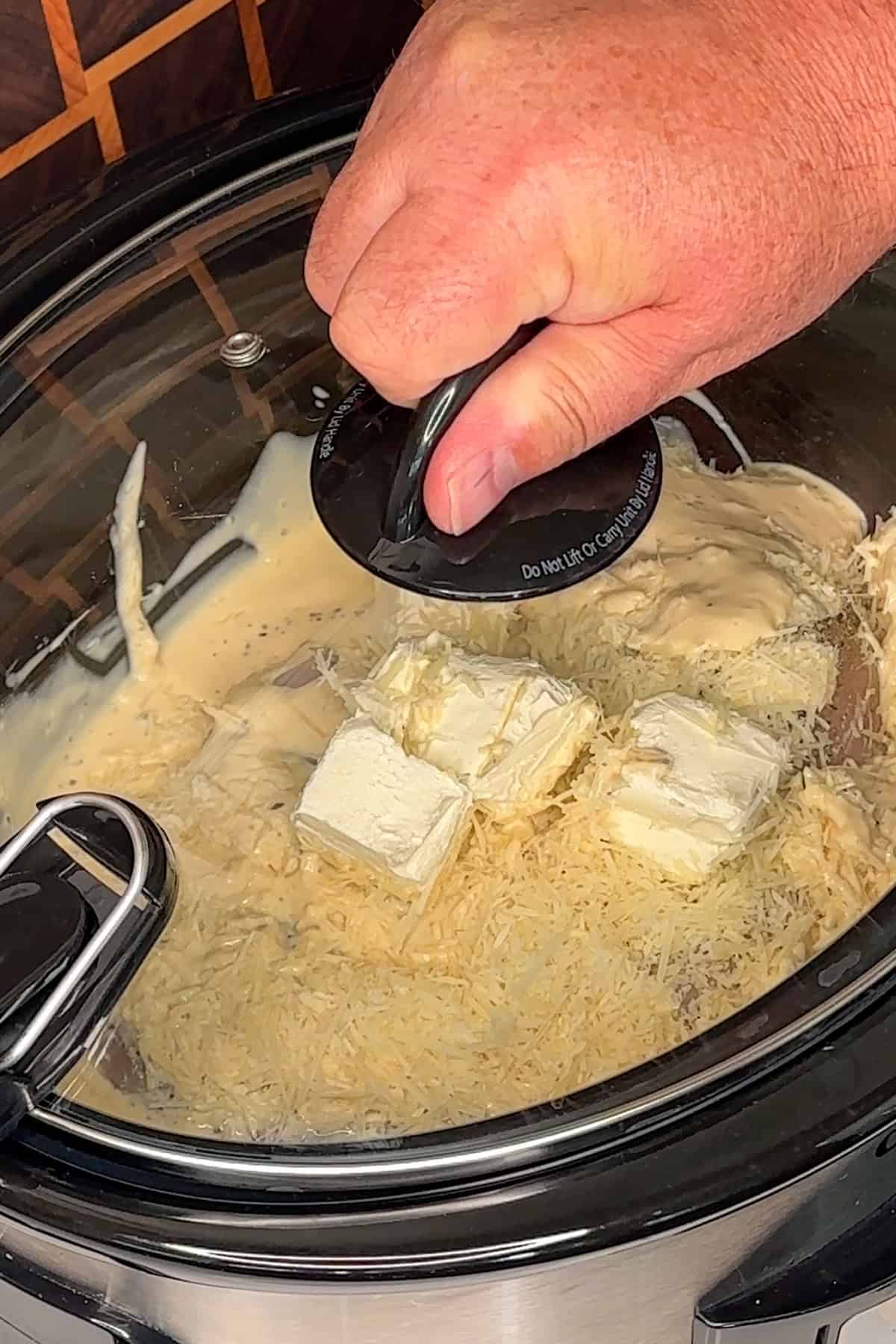 A hand putting a lid on a crock pot.