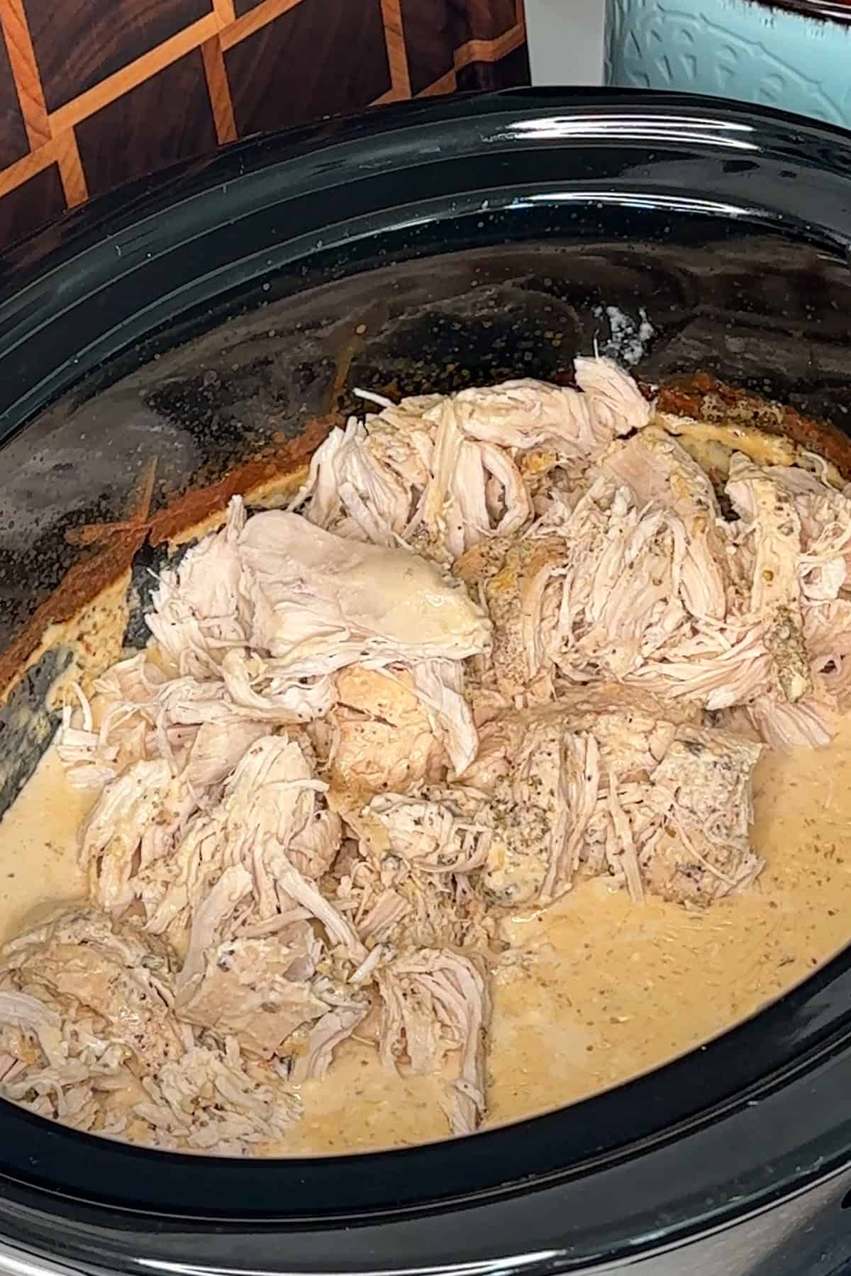 Shredded chicken added to alfredo sauce in a crock pot.